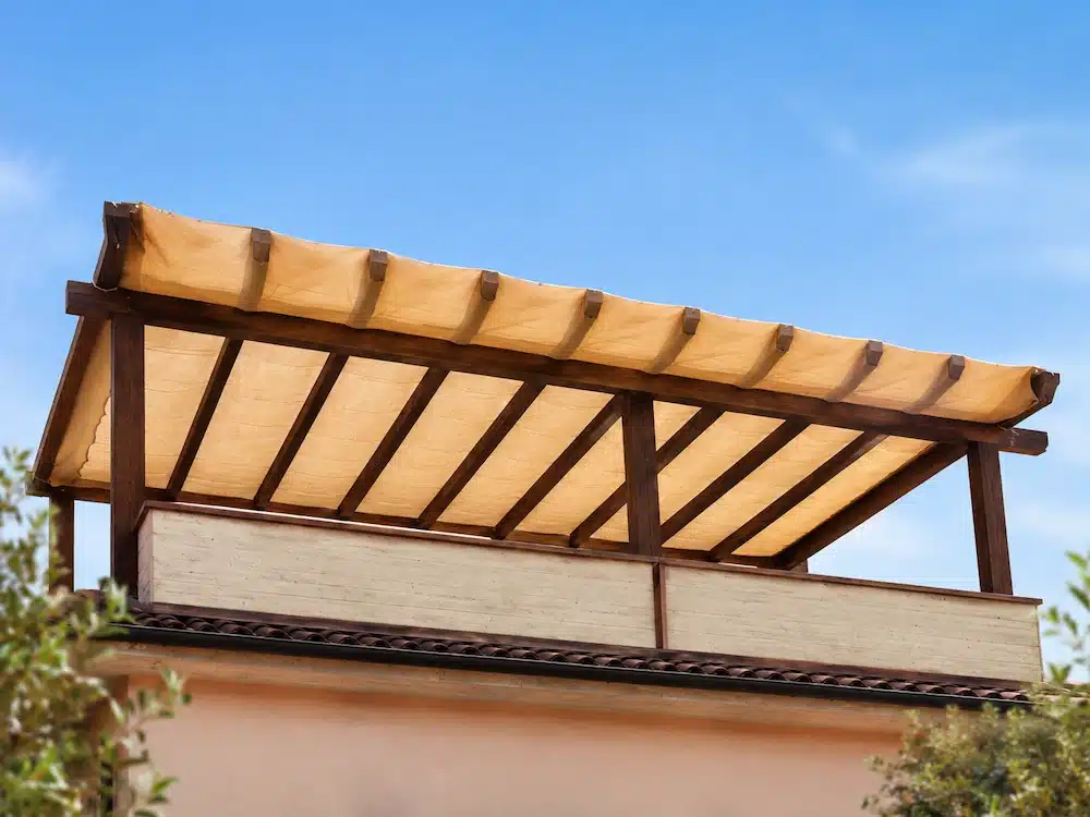 Telo ombreggiante beige su misura installato su pergola in legno con bordatura e occhielli