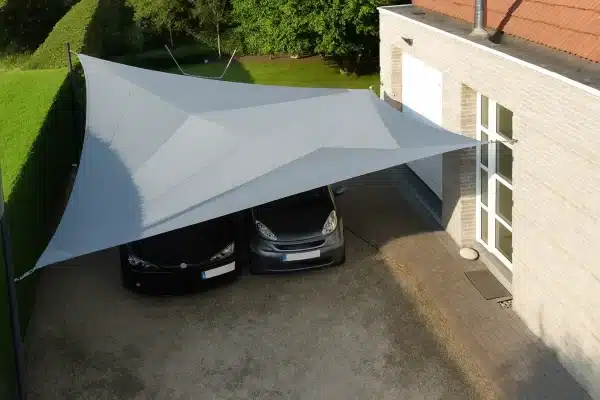 Vela ombreggiante grigia montata su parcheggio per auto accanto a casa in muratura