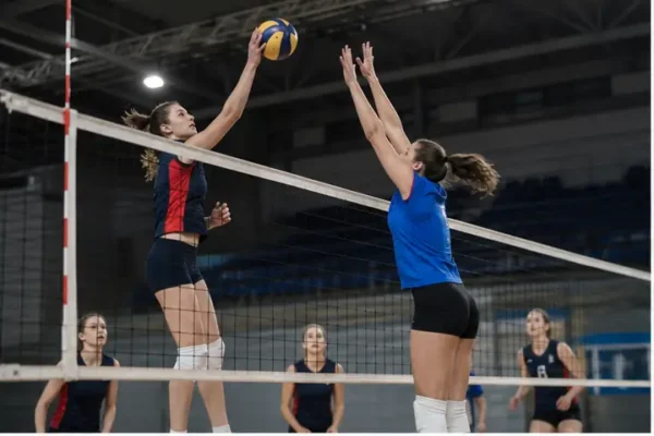 Atlete in azione a rete durante una partita di pallavolo indoor.