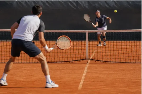 Tennisti in azione con rete regolamentare su campo in terra battuta.